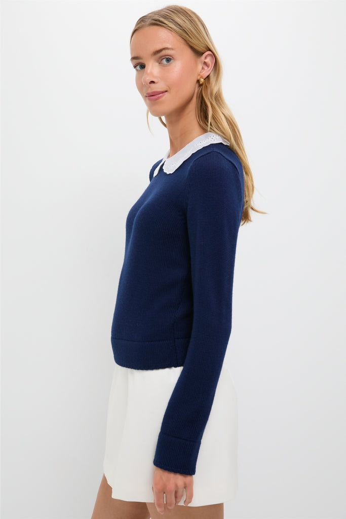 Young woman in profile wearing the classic Navy Violette Sweater with an eyelet-detailed collar, effortlessly paired with a white skirt and gold hoop earrings.