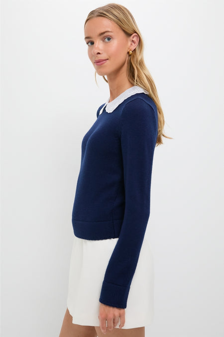 Young woman in profile wearing the classic Navy Violette Sweater with an eyelet-detailed collar, effortlessly paired with a white skirt and gold hoop earrings.