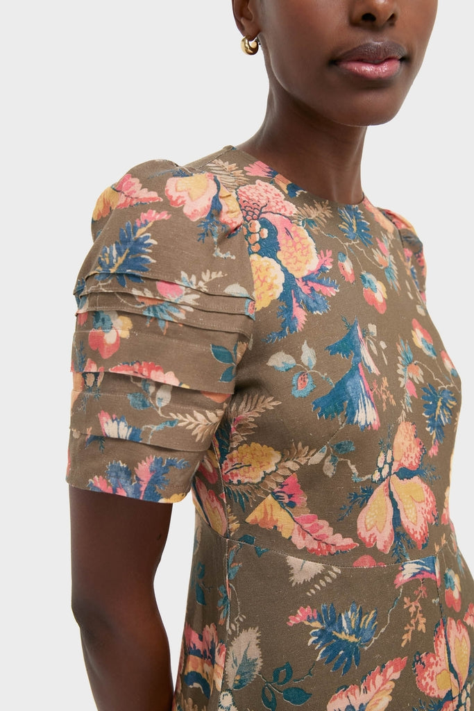 Person wearing the Olive Floral Casey Dress with a high neck, featuring pink, yellow, and blue all-over floral print and pleated sleeves, paired with a gold hoop earring.