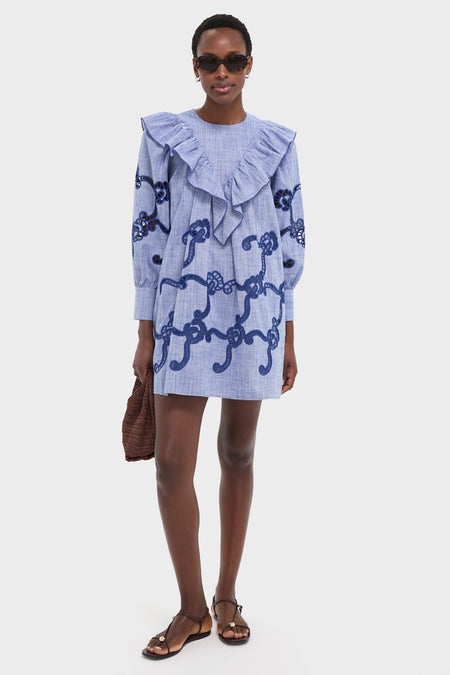 Model wearing the Seabank Chambray Azalea Dress with a ruffled collar and rope motif, exuding a classic, effortless style. Paired with sunglasses and a woven handbag for high-end fun.