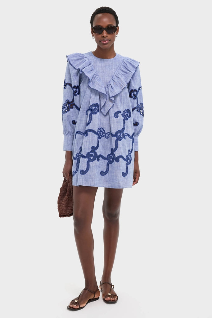 Model wearing the Seabank Chambray Azalea Dress with a ruffled collar and rope motif, exuding a classic, effortless style. Paired with sunglasses and a woven handbag for high-end fun.