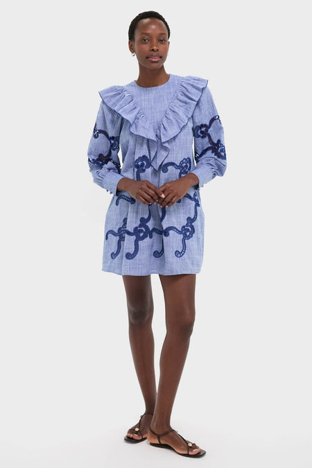 Woman in Seabank Chambray Azalea Dress, featuring a classic, effortless style with ruffled V-collar and embroidered swirls for a high-end, fun look.