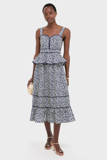 Model wearing the classic Vine Stripe Lacey Dress, a high-end blue-and-white midi with a peplum waist and tiered ruffled hem, styled effortlessly with a clutch.