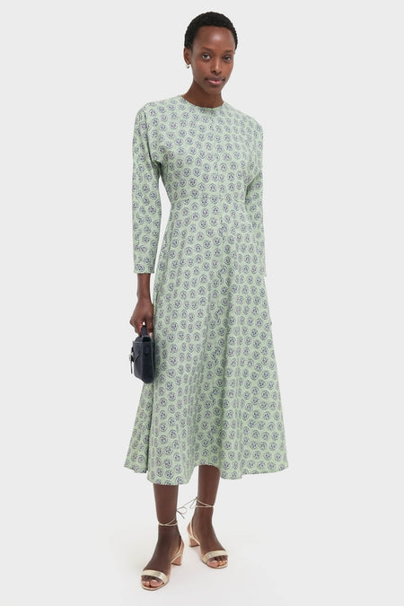 Model in Navy Bird Block Vika Dress, a classic, long-sleeved pale green dress with dark-blue motifs, holding a navy handbag, embodying effortless, high-end style.