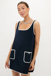Young woman models the Navy Mini Terrycloth Button Tank Dress, featuring a classic, effortless design with white trim, patch pockets, and elegant gold accessories, embodying a fun, high-end style.