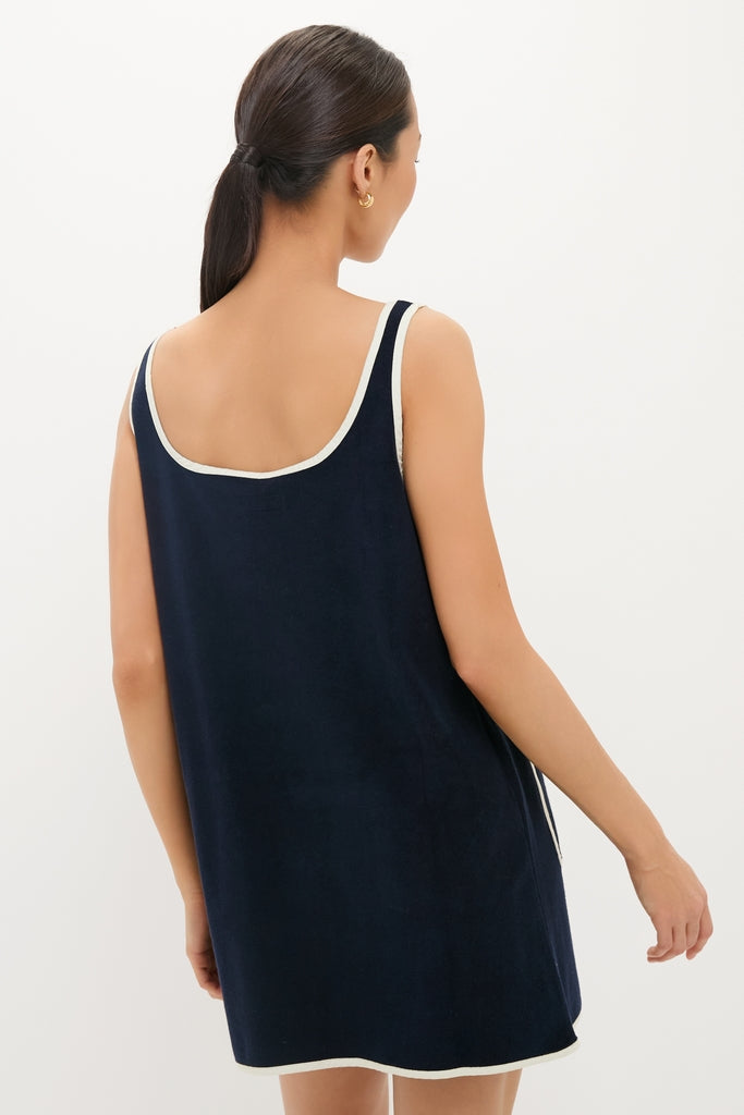 Woman in a classic Navy Mini Terrycloth Button Tank Dress with white trim, embodying an effortless and high-end style. Her hair is in a low ponytail, accessorized with gold hoop earrings.
