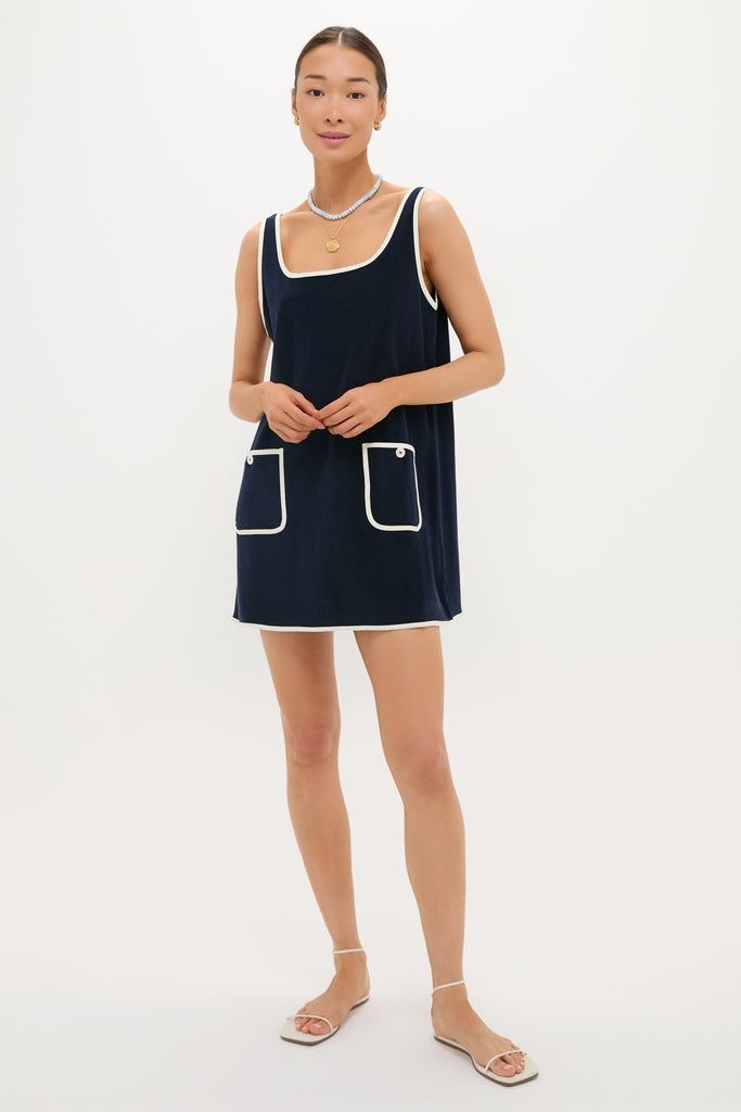 Model wearing Navy Mini Terrycloth Button Tank Dress with contrast trim, square neckline, and front pockets. Paired with gold jewelry and white sandals, exuding classic, effortless, high-end style.