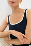 Woman in a classic, sleeveless Navy Mini Terrycloth Button Tank Dress, effortlessly styled with white trim, small gold hoops, and pale pink manicured nails, embodying Tuckernuck's fun, high-end fashion.