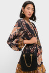 Woman in a bohemian dress holds a classic Black Small Macrame Veronica Beard Slouch Bag with gold chain straps, exuding effortless high-end style and fun elegance.