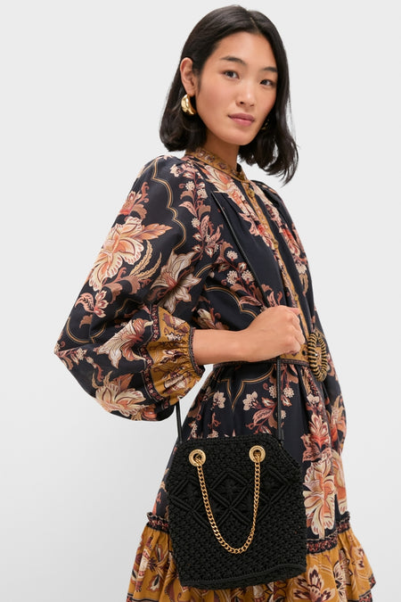 Woman in a bohemian dress holds a classic Black Small Macrame Veronica Beard Slouch Bag with gold chain straps, exuding effortless high-end style and fun elegance.