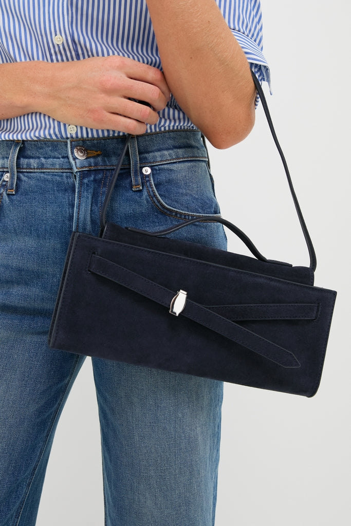 Woman holding the Navy Suede Veronica Beard Dash Clutch, a classic, high-end rectangular bag with a flap closure, silver-tone clasp, and decorative suede belt detail.
