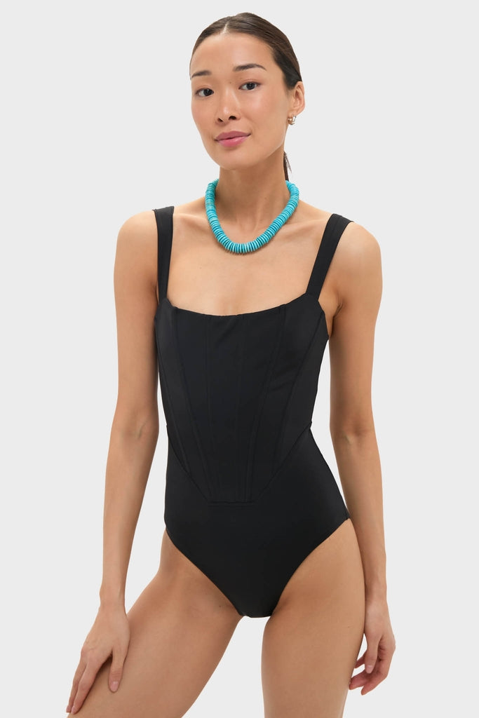 Black Adelaide One Piece swimsuit with corset-style boning, wide straps, and a chunky turquoise necklace. Classic, effortless style for fun, high-end beach days.
