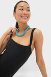 Woman in classic Black Adelaide One Piece swimsuit with corset-style boning, accessorized with a turquoise necklace, showcasing an effortless, high-end style.