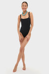 Model in classic Black Adelaide One Piece swimsuit with square neckline and turquoise necklace, exuding high-end, effortless style and fun confidence.