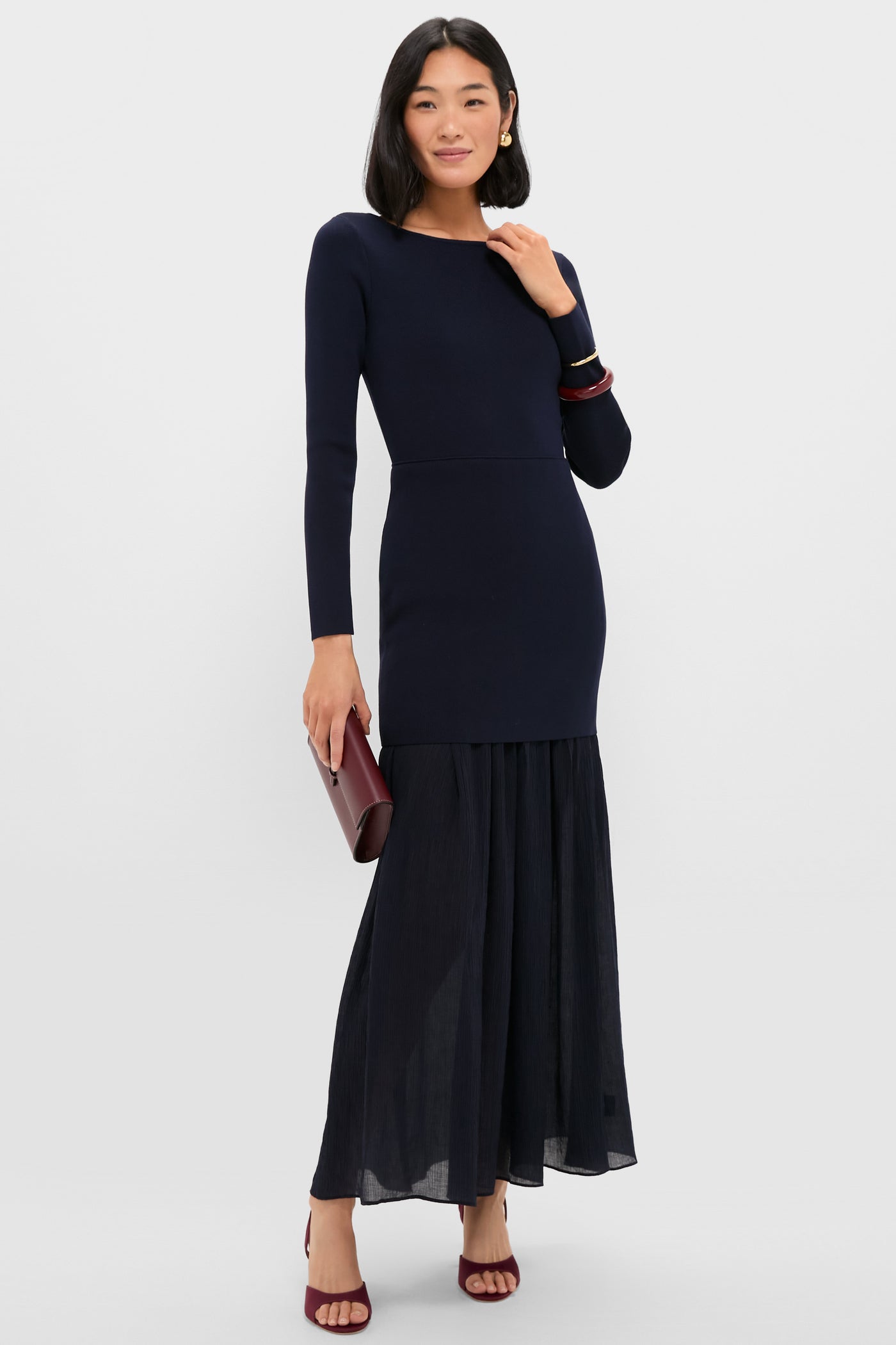 Model showcases the classic Mulberry Brigitte Heel, a high-end, effortless design in satin and leather, paired with a pleated skirt and burgundy clutch.