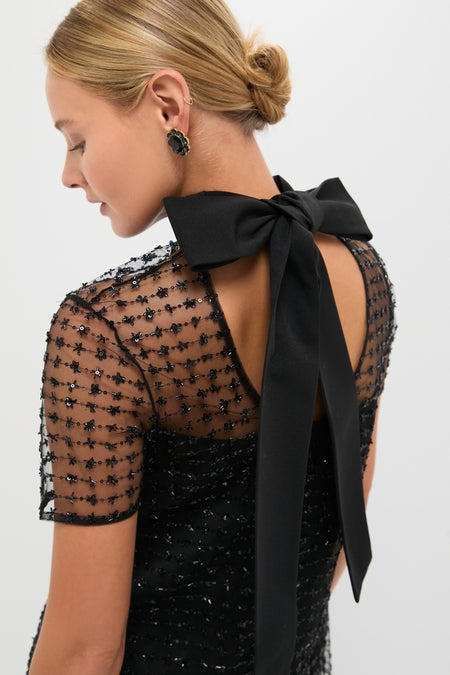 Elegant woman in Stardust Onyx Ilana Dress, featuring a classic sheer overlay with sequins and a self-tie bow, embodying effortless, high-end style.