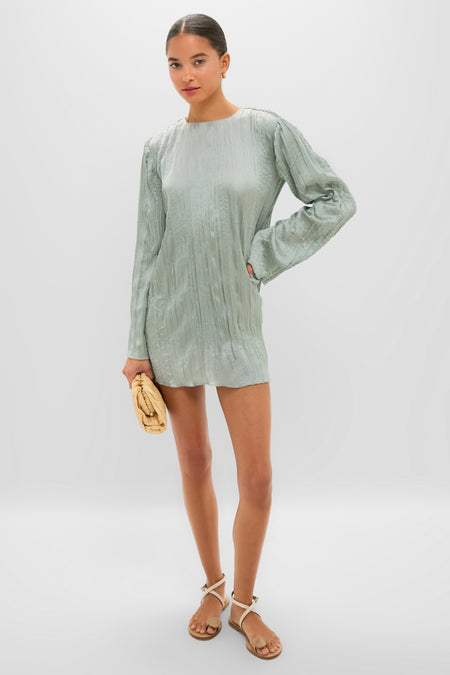 Woman modeling the Silver Sage Kona Dress, a classic mini with long sleeves and textured fabric, paired with a tan clutch and white sandals for an effortless, high-end look.