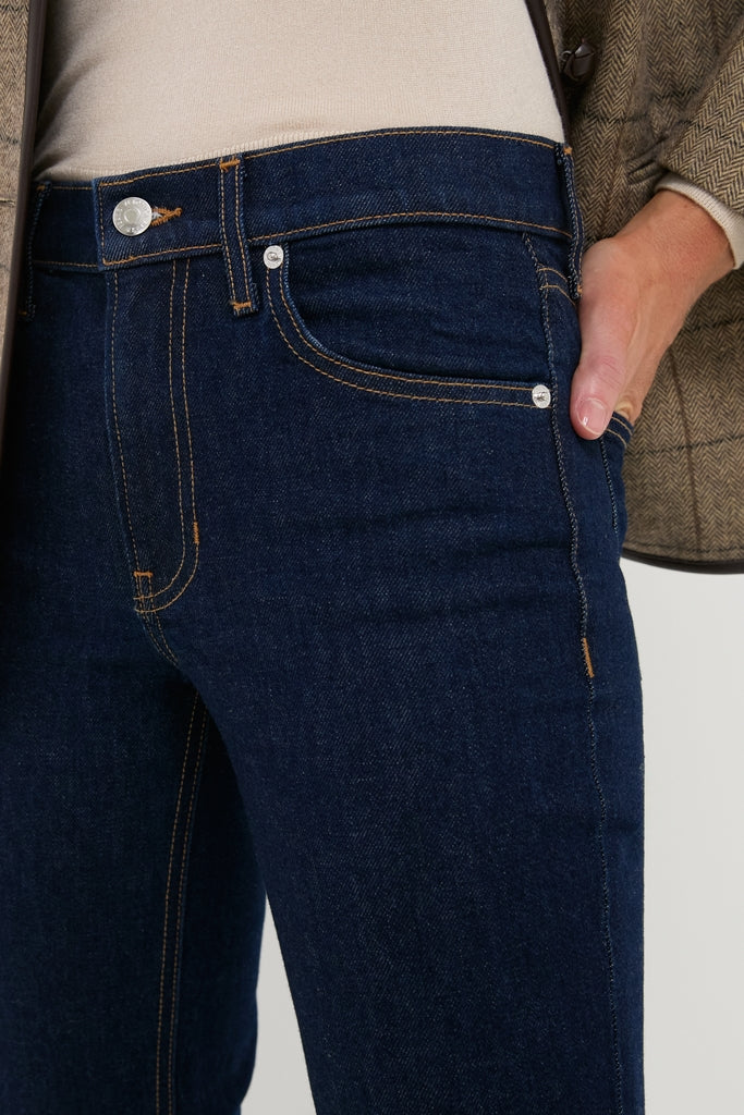 Indigo Rinse Leah Mid Rise Straight Leg jeans, showcasing a classic five-pocket design with effortless style. Paired with a tucked beige top and tweed jacket for a high-end, fun look.