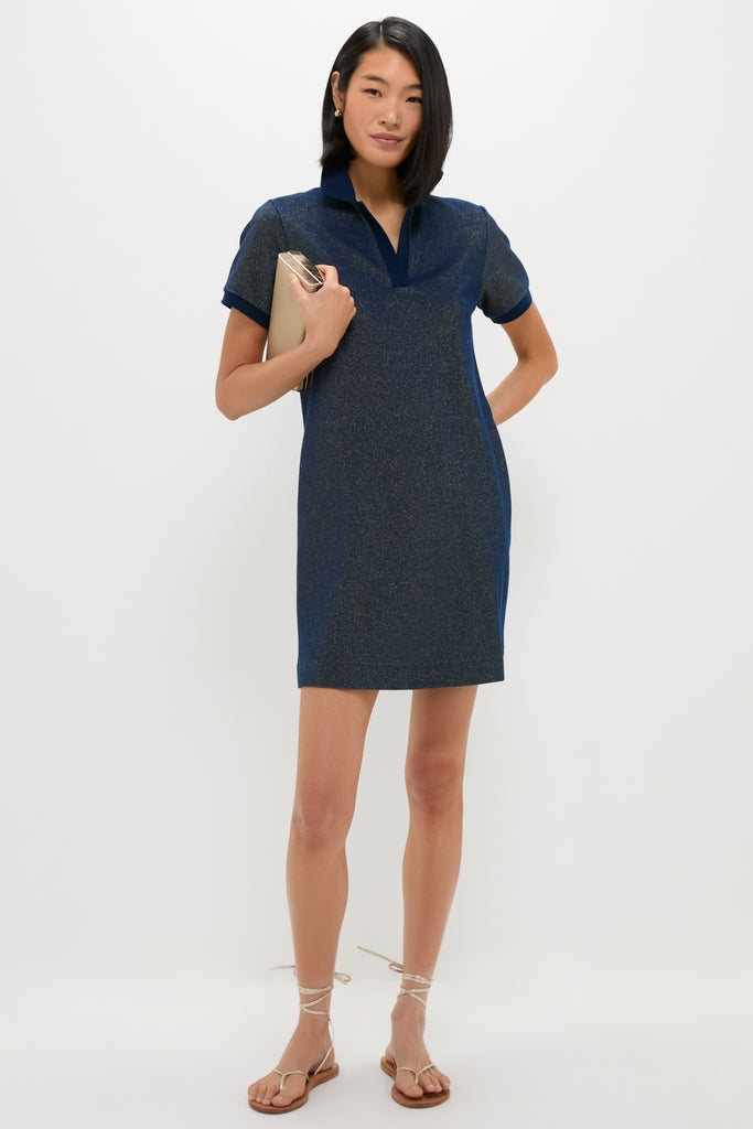 Woman in a Navy Gold Lurex Pique Hutton Dress holding a beige clutch, embodying classic and effortless style with fun, high-end details, perfect for any occasion.