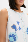 Woman in classic Folk Flower Embroidered Luna Top featuring effortless white, sleeveless design with fun pale blue rickrack trim and high-end blue floral embroidery.