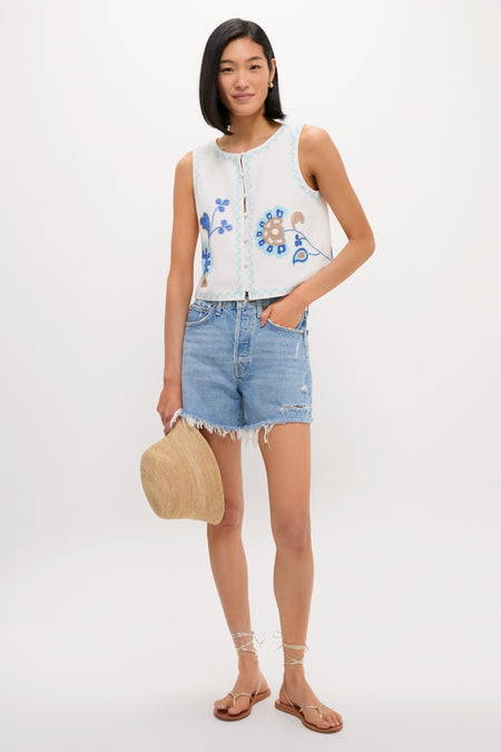 Model wearing the classic Folk Flower Embroidered Luna Top with floral details, paired with frayed denim shorts and strappy sandals, exuding an effortless, high-end summer style.