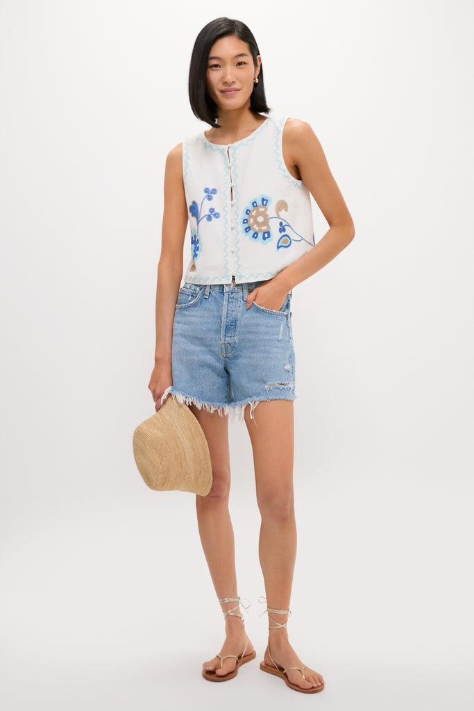 Model wearing the classic Folk Flower Embroidered Luna Top with floral details, paired with frayed denim shorts and strappy sandals, exuding an effortless, high-end summer style.