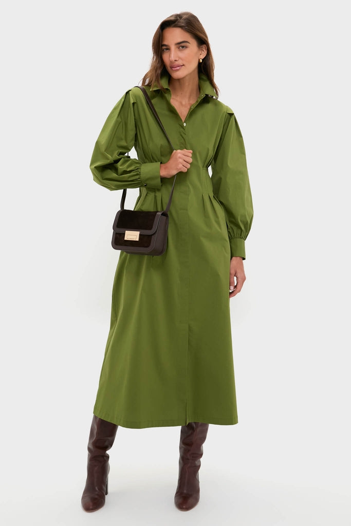 Model wearing the classic Fern Corinne Dress, an olive-green, button-front shirt dress with a tailored waist, styled effortlessly with knee-high boots and a chic crossbody bag.