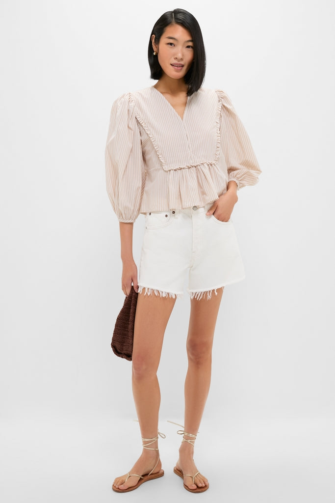 Young woman models the Natural Stripe Stevie Blouse, a classic, effortless pinstriped top with ruffle trim and peplum hem, paired with high-waisted shorts and strappy sandals.