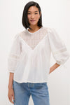 Woman wearing the White Bella Blouse, a classic and effortless piece with eyelet detailing, ¾-length puff sleeves, and a relaxed fit, paired with medium-wash jeans.