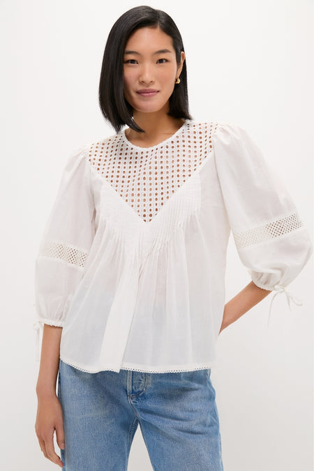 Woman wearing the White Bella Blouse, a classic and effortless piece with eyelet detailing, ¾-length puff sleeves, and a relaxed fit, paired with medium-wash jeans.