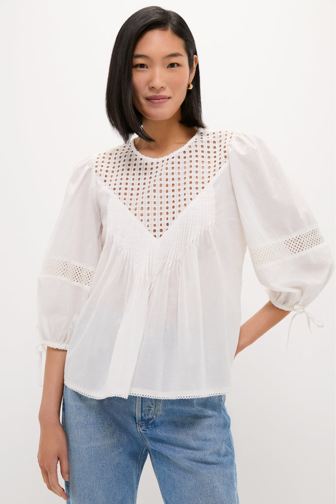 Woman wearing the White Bella Blouse, a classic and effortless piece with eyelet detailing, ¾-length puff sleeves, and a relaxed fit, paired with medium-wash jeans.
