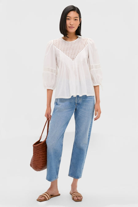 Woman wearing the classic White Bella Blouse with eyelet detailing, paired effortlessly with light-blue jeans, woven sandals, and a straw tote for a fun, high-end look.