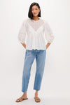 Young woman in a classic, effortless White Bella Blouse with eyelet details, paired with high-waisted jeans and woven sandals, embodying a fun, high-end style.