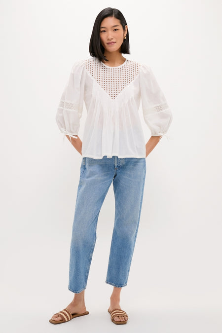 Young woman in a classic, effortless White Bella Blouse with eyelet details, paired with high-waisted jeans and woven sandals, embodying a fun, high-end style.