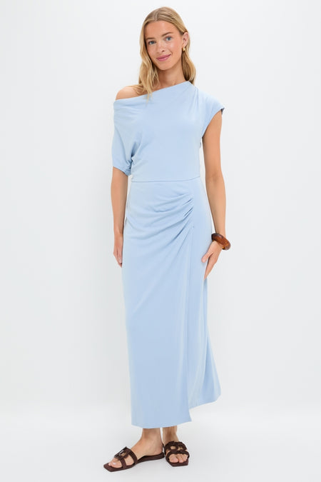 Young woman models the Blue Fog Faux Wrap Senna Dress, showcasing its classic, effortless drape and fun, high-end style, paired with brown sandals and a wooden bangle.