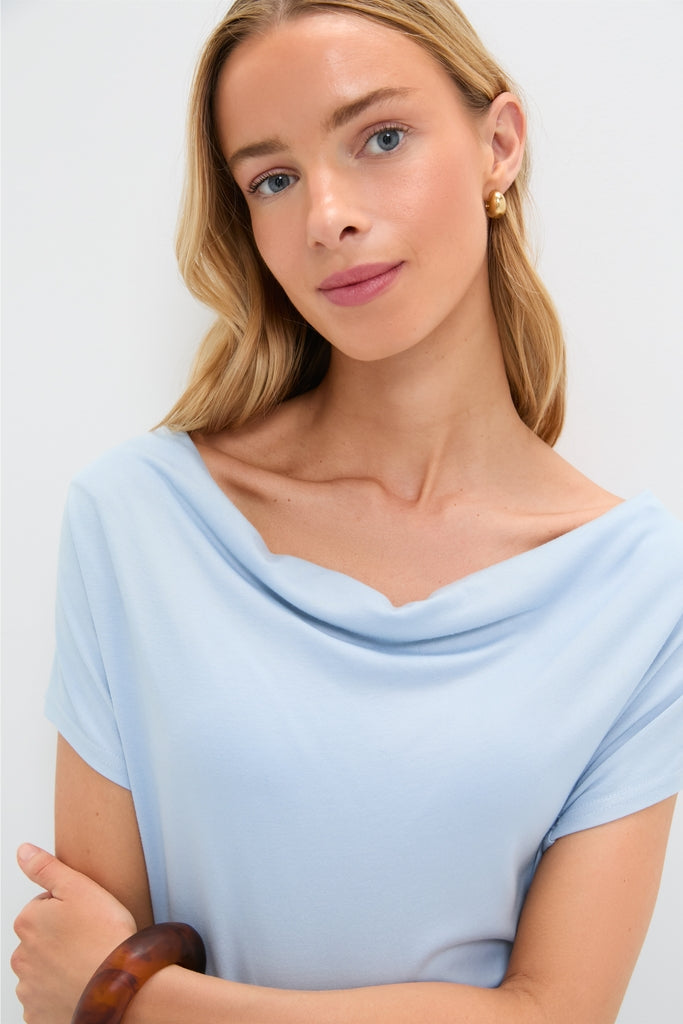 Young woman in a Blue Fog Faux Wrap Senna Dress, showcasing classic elegance with an effortless, high-end look, accented by a tortoiseshell bangle and gold hoop earring.