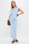 Model in the Blue Fog Faux Wrap Senna Dress, a classic, effortless maxi with one-shoulder design, ruched detail, wooden bangle, and knitted clutch, exuding high-end style.