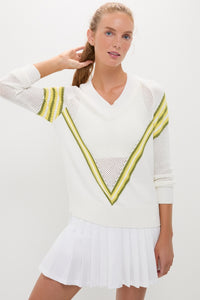 Young woman wearing the Yellow Emaline V-Neck Pullover with chevron stripes, paired with a pleated mini skirt, exuding a classic, effortless, and fun high-end style.