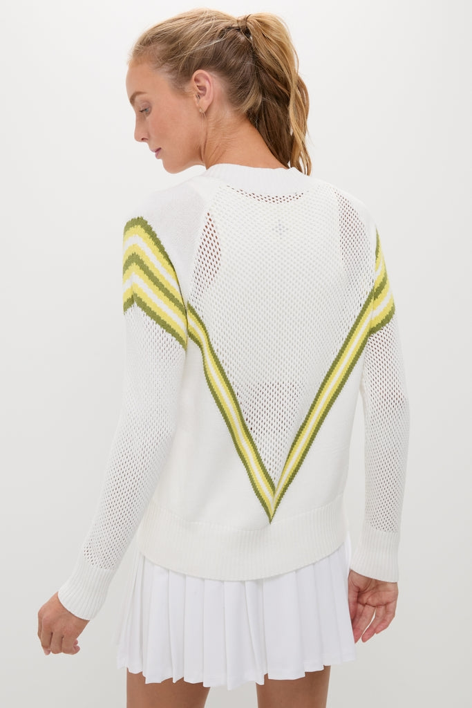 Model in Yellow Emaline V-Neck Pullover with chevron stripes, paired with a pleated mini-skirt, showcasing an effortless, classic style in a high-end, fun design.
