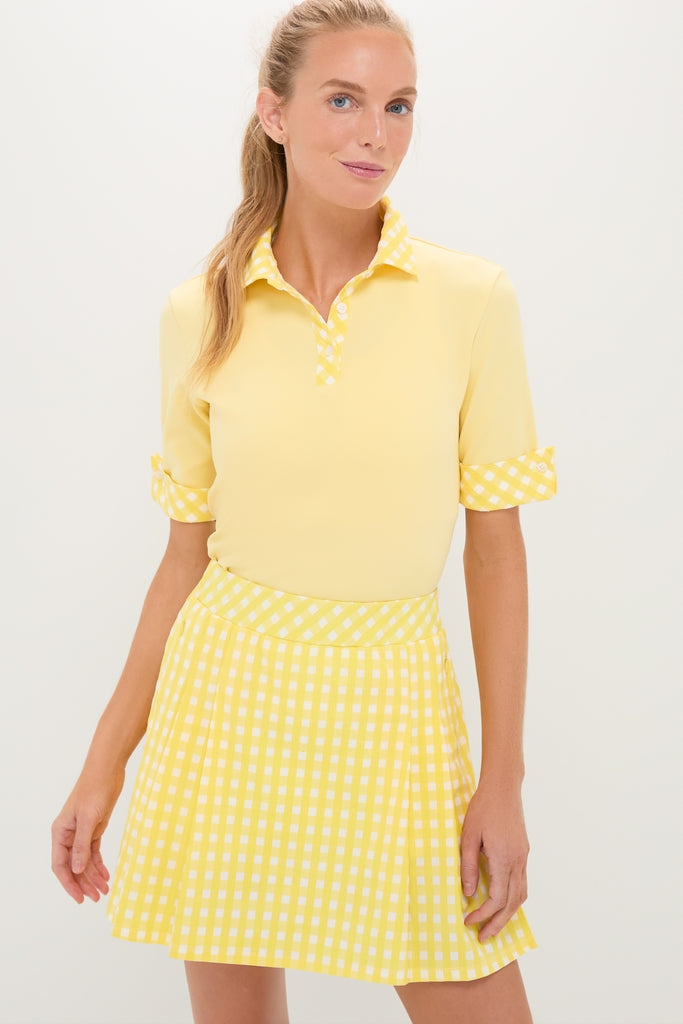 Woman models the Lemon Yellow Prynn Polo with classic rolled sleeves and gingham accents, paired effortlessly with a fun, high-end matching pleated mini-skirt.