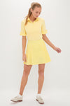 Woman models the classic Yellow Gingham Performance Jersey Park Golf Skirt, featuring pleats, high rise, and side pockets, paired effortlessly with a sporty yellow polo top.