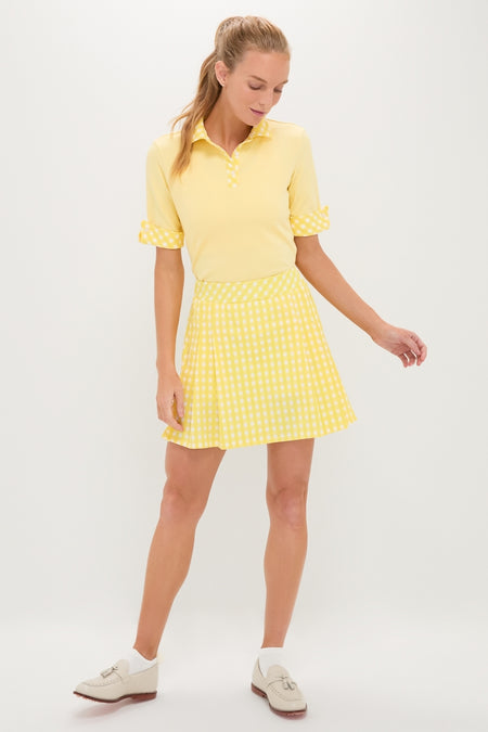 Woman models the classic Yellow Gingham Performance Jersey Park Golf Skirt, featuring pleats, high rise, and side pockets, paired effortlessly with a sporty yellow polo top.