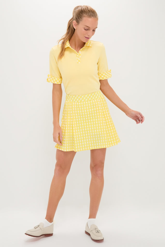 Woman models the classic Yellow Gingham Performance Jersey Park Golf Skirt, featuring pleats, high rise, and side pockets, paired effortlessly with a sporty yellow polo top.