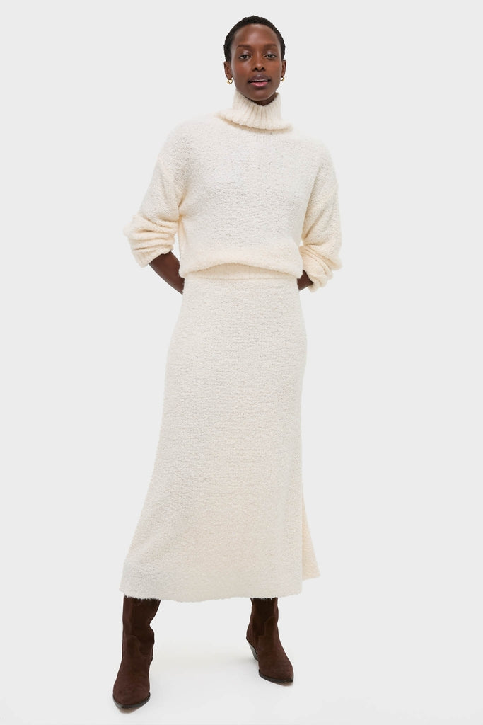 Woman models the classic Ivory Boucle Lillia Sweater Skirt, showcasing a high-end, effortless style with a cozy, textured knit, paired with matching turtleneck and suede boots.