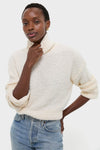 Woman in Ivory Boucle Whilden Sweater Top, showcasing a classic, effortless look with a chunky turtleneck and ribbed finishes, embodying fun and high-end style.