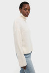 Dark-skinned model in Ivory Boucle Whilden Sweater Top, showcasing its classic, effortless turtleneck design with ribbed finishes, paired with light-blue jeans for a fun, high-end look.