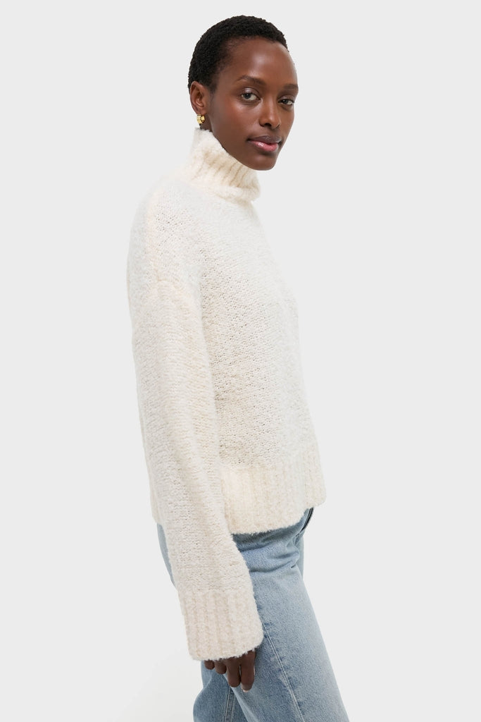 Dark-skinned model in Ivory Boucle Whilden Sweater Top, showcasing its classic, effortless turtleneck design with ribbed finishes, paired with light-blue jeans for a fun, high-end look.