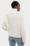 Person in a classic Ivory Boucle Whilden Sweater Top with chunky turtleneck and ribbed finishes, paired with jeans, showcasing an effortless, high-end winter look.