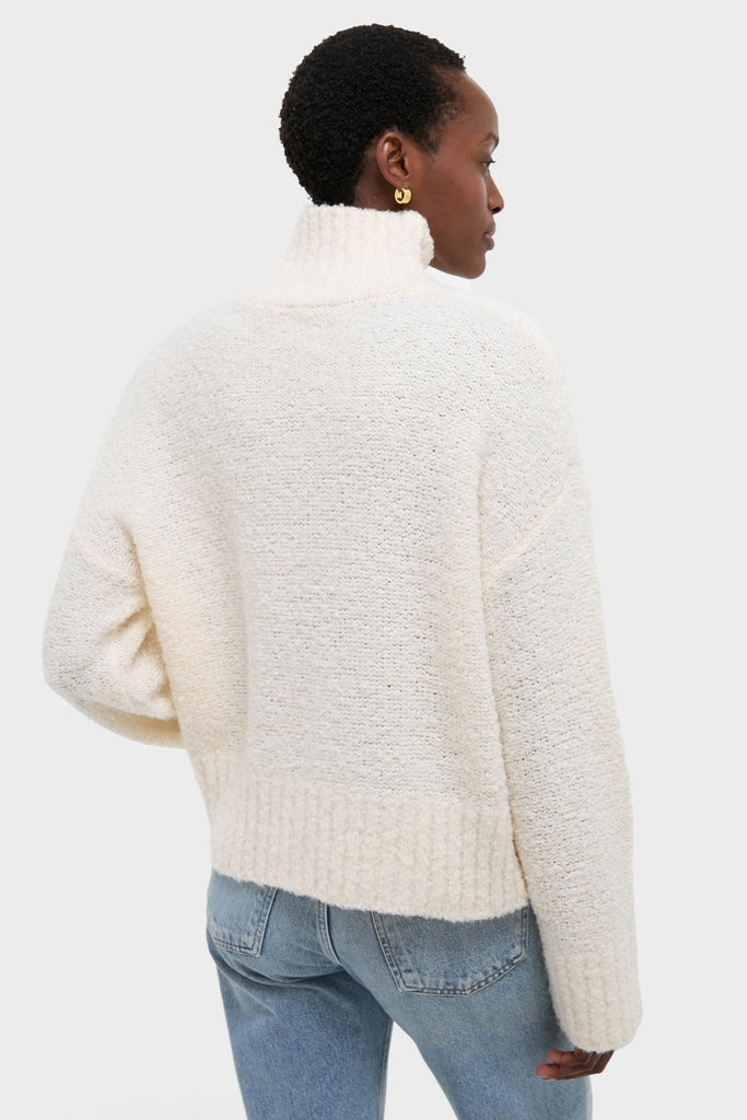 Person in a classic Ivory Boucle Whilden Sweater Top with chunky turtleneck and ribbed finishes, paired with jeans, showcasing an effortless, high-end winter look.
