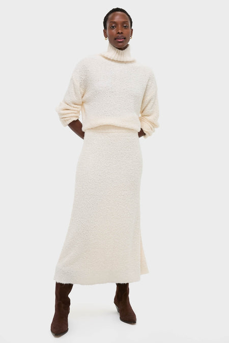 Woman in Ivory Boucle Whilden Sweater Top and matching skirt, showcasing a classic, effortless winter look with relaxed turtleneck and ribbed finishes, paired with dark suede boots.